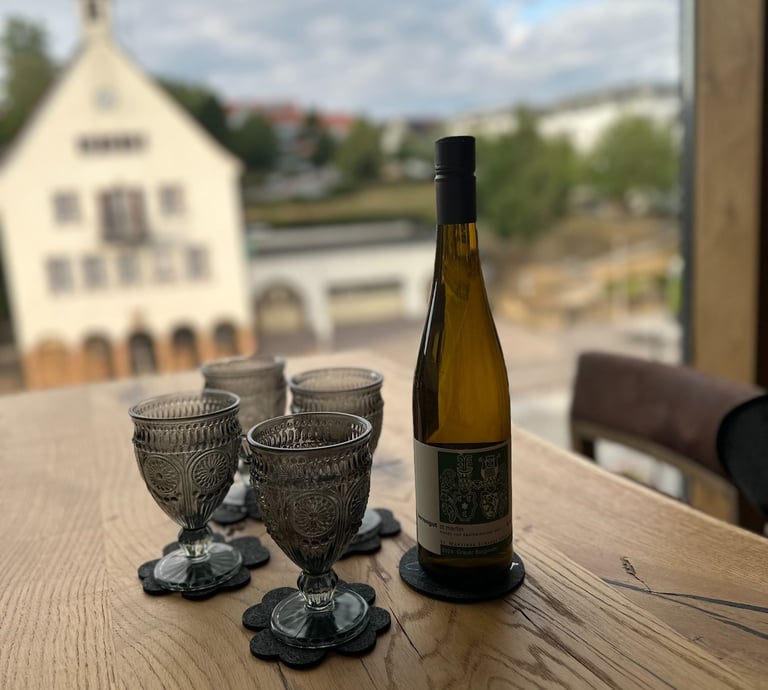 Eine Flasche Wein mit 4 Gläsern - im Hintergrund das alte Wernauer Rathaus