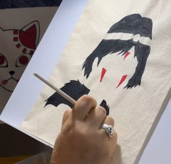 Artista pintando a mano un personaje de anime de La Princesa Mononoke sobre una tote bag de lino