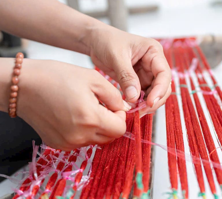 Artisan hands skillfully tying red silk threads on a traditional ikat weaving loom.