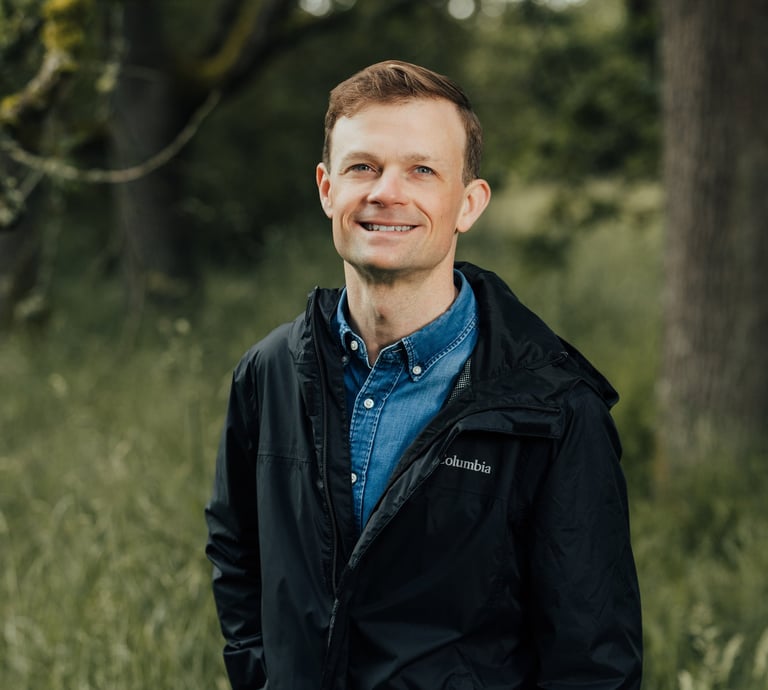 Jesse Robertson in a blue collared shirt and black rain jacket in a Garry Oak meadow.