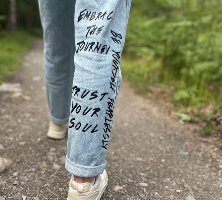 An image of someone's leg walking in nature, with empowering quotes written on the jeans