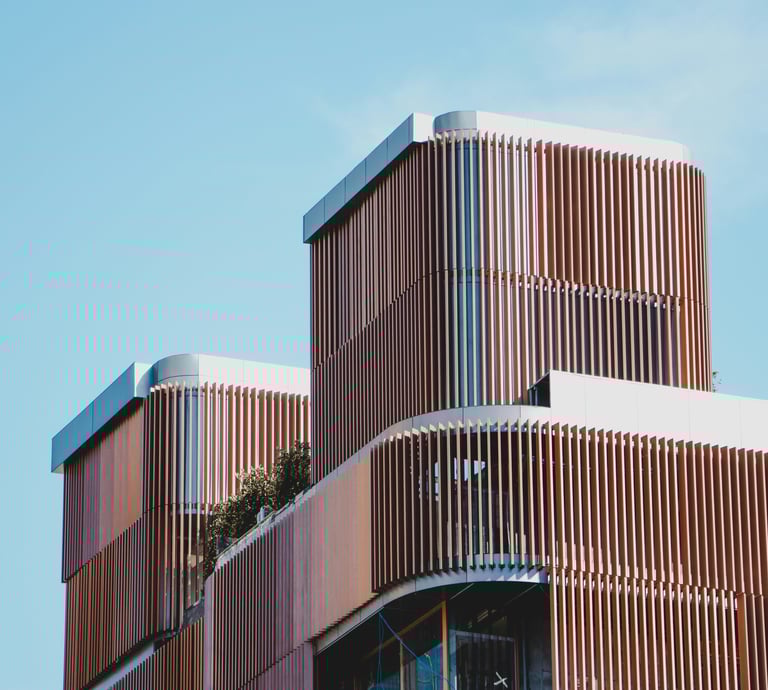 Edificio moderno construido con hormigón, vidrio y revestimiento de madera, con mucha vegetación.