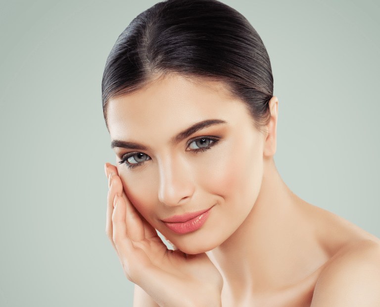 woman with green eyes and clear skin smiling with hand on cheek