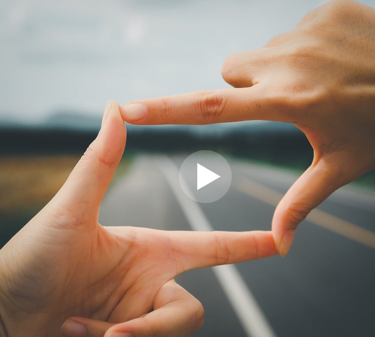 person's fingers making a rectangle with a "play" button in the middle against background of road