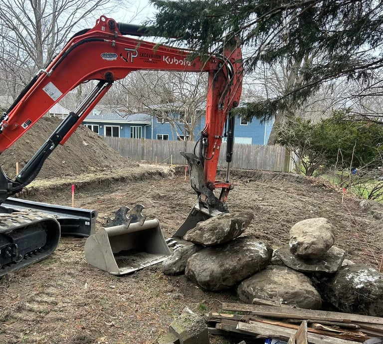 Orange Kubota excavator moving large boulders for a backyard landscape retaining wall project.