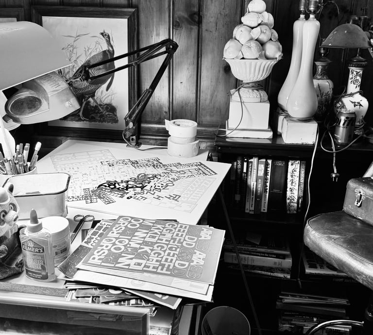 Cluttered artist's workspace with vintage desk supplies, art prints, and a leather chair in black and white.
