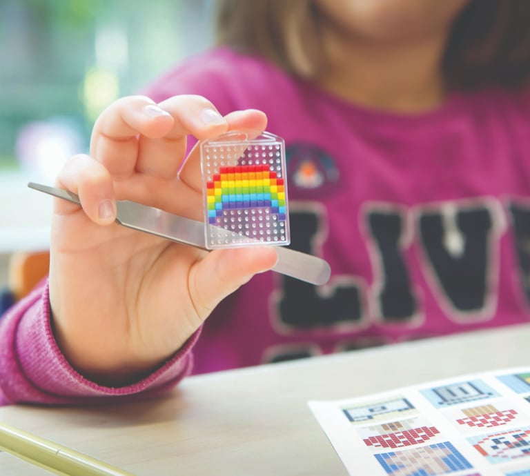 A girl showing colorful rainbow picture on transparent baseplate she made from pixel squares