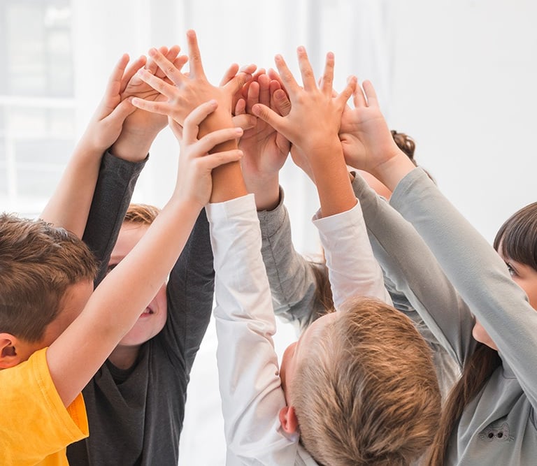 Kinder in der Spielgruppe der Zukunft heben gemeinsam die Hände – Förderung von Teamgeist und sozial