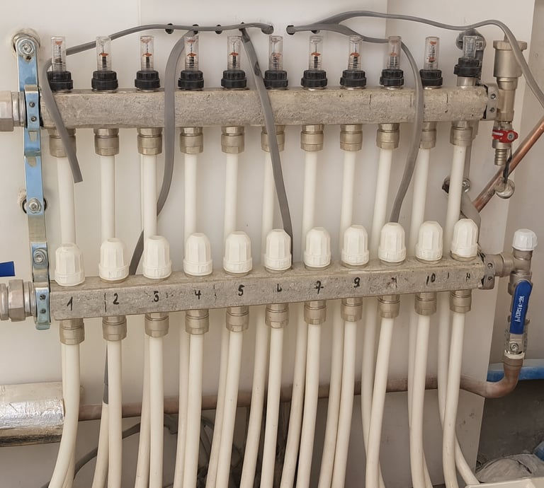 Verdeler voor centrale verwarming met witte leidingen en regelventielen – installatie in Leuven