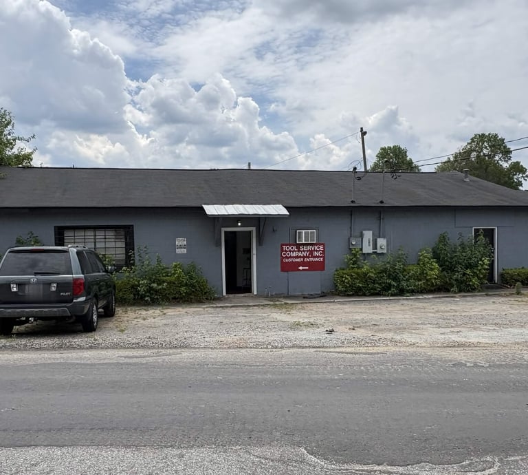 Tool Service Company building with a dark SUV parked in front under a cloudy sky.