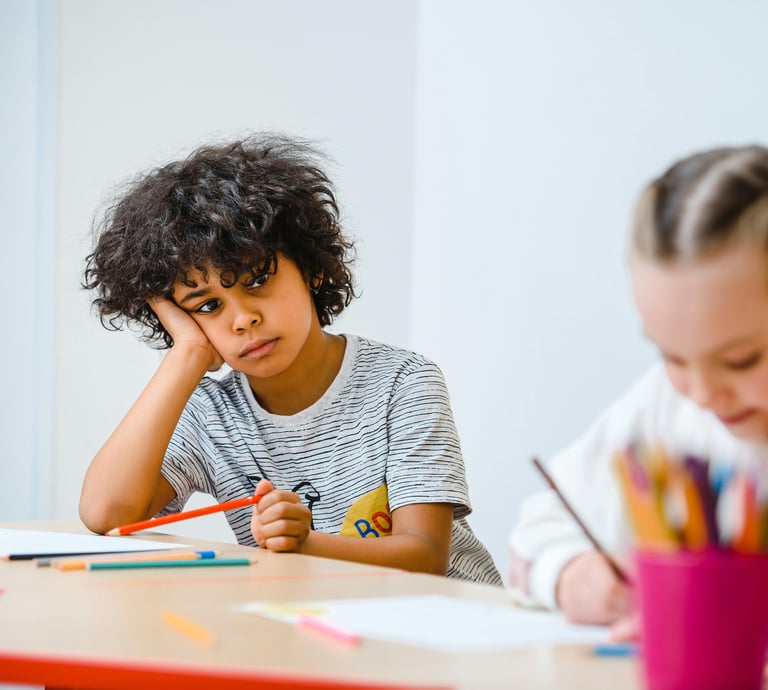 Criança com expressão de desatenção e cansaço em sala de aula, ilustrando dificuldades escolares e sintomas de TDAH.