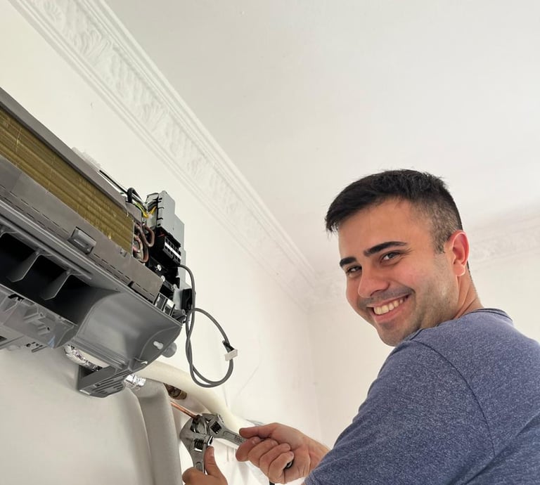 A smiling technician uses an adjustable wrench to repair an indoor wall-mounted air conditioning unit.
