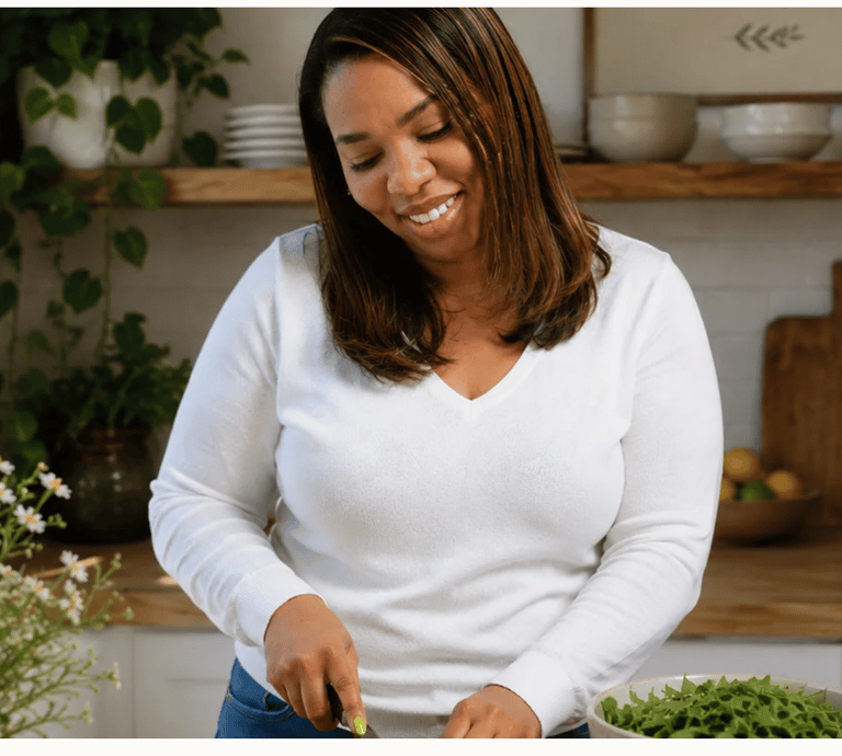 A smiling woman preparing a healthy salad with fresh greens in a bright, modern kitchen.