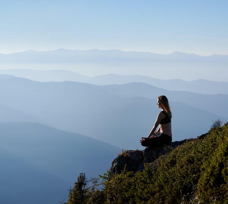 Panoramic image of a mountainous environment with a young woman meditating in the foreground