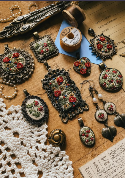 Pendientes y joyería florales bordados a mano en marcos de bronce vintage sobre una mesa de madera