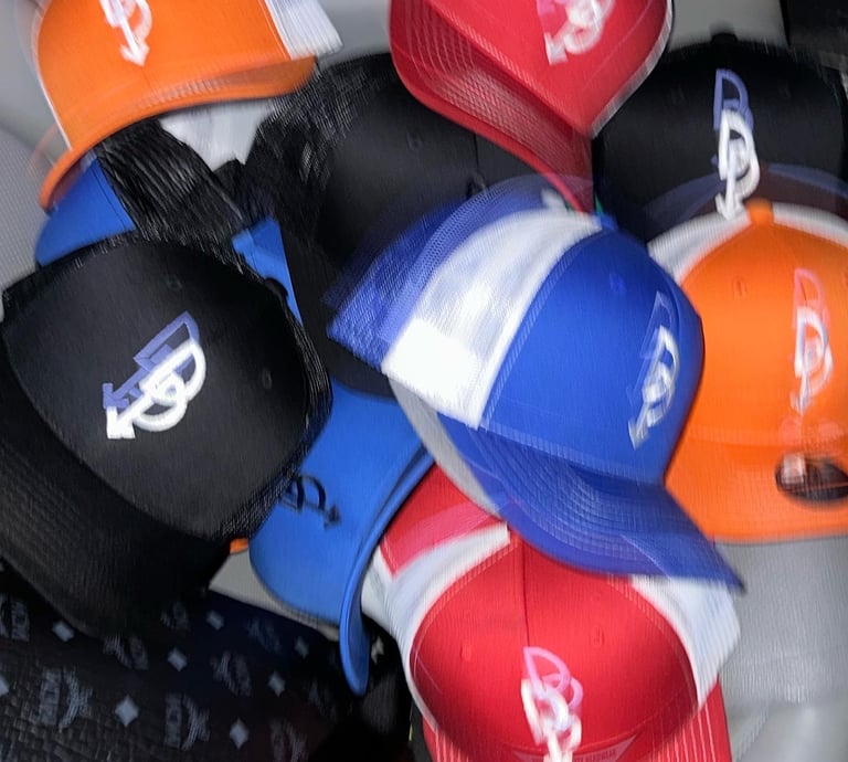 A pile of assorted colorful trucker hats and snapback caps with embroidered logos in blue, red, and orange.