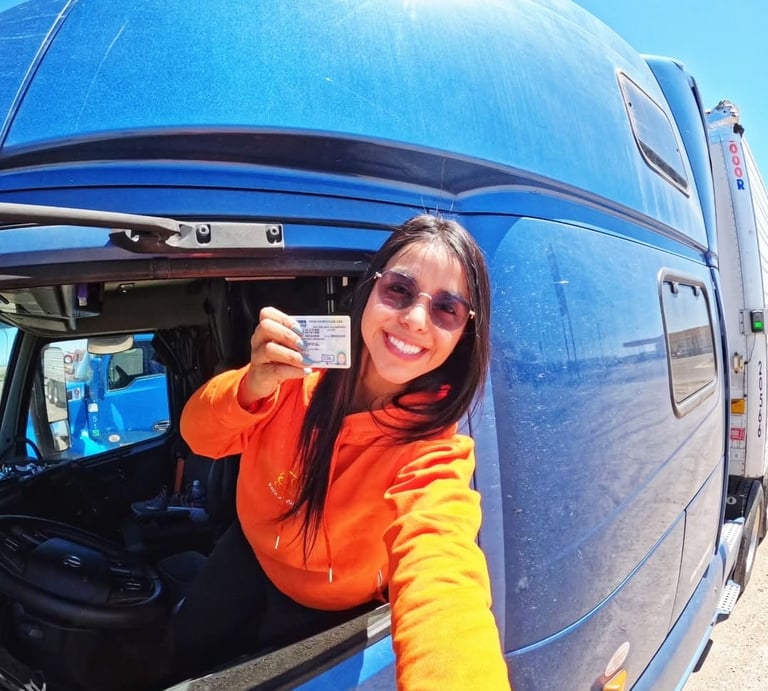 Conductora de camión sonriente sosteniendo su licencia CDL desde la cabina de un camión