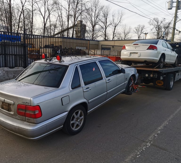 A scrap Volvo car being towed by a tow truck