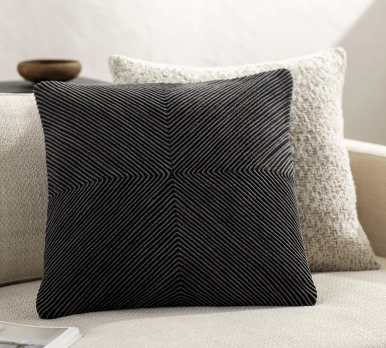 Modern black decorative throw pillow with a geometric ribbed texture on a white sofa.