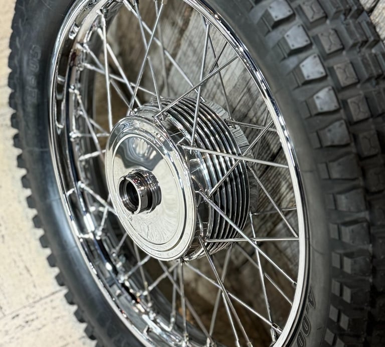 a motorcycle vintage hand polished wheel with a knobbie tire in front of wooden wall.