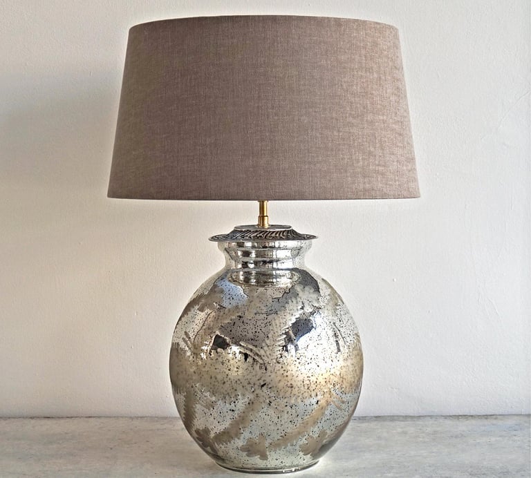 a silver mercury glass vase with a lamp on a table