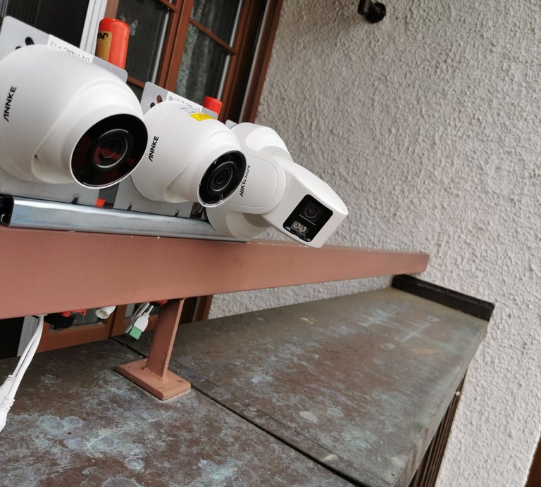 Multiple outdoor security cameras including Annke and Hikvision brands mounted on an exterior wall.