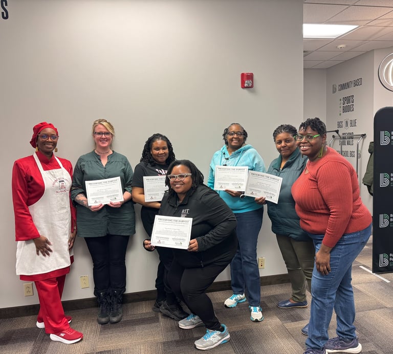 Seven women smiling while holding training certificates during a community partnership graduation event.