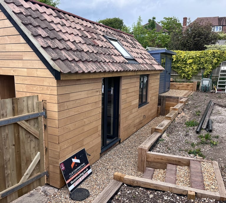 Side exterior of Brighton garage conversion with sweet chestnut cladding, black doors and oak retain