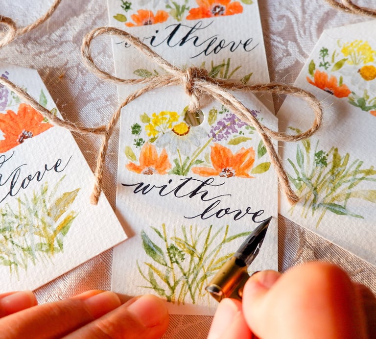 a calligrapher writing the words “with love” for a gift tag with handmade watercolor florals