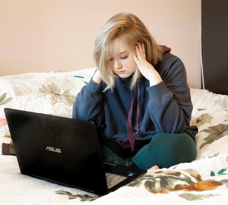 Garota jovem sentada de forma confortável, olhando para a tela de um laptop, triste