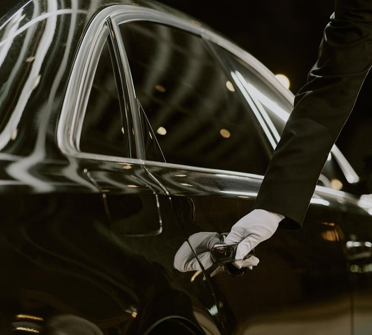 A chauffeur in white gloves opening the door of a black luxury car for executive transport.VIREMONT 