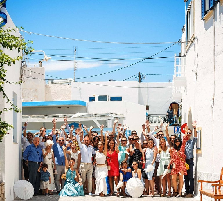 Foto di gruppo di tutti gli invitati del matrimonio che salutano verso il fotografo, nel bianco dell'isola greca Antiparos