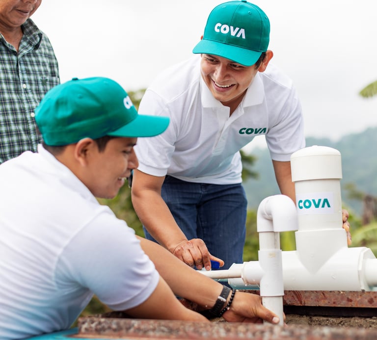 Two male workers with COVA hats, working on a PVC pipe water system.