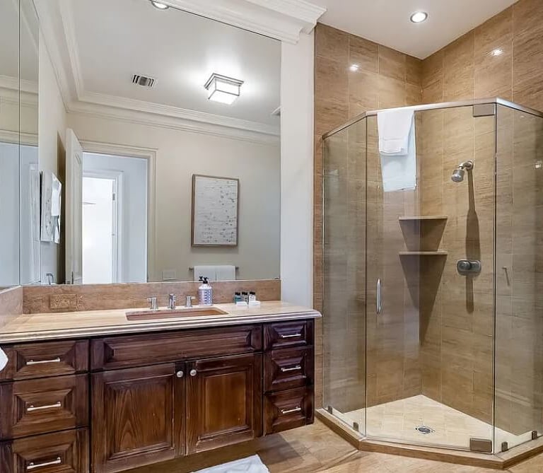 Bathroom remodel with a wood vanity, stone countertop, and glass-enclosed shower.