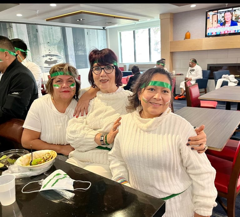 Three women in white sweaters and green headbands celebrating at a restaurant.