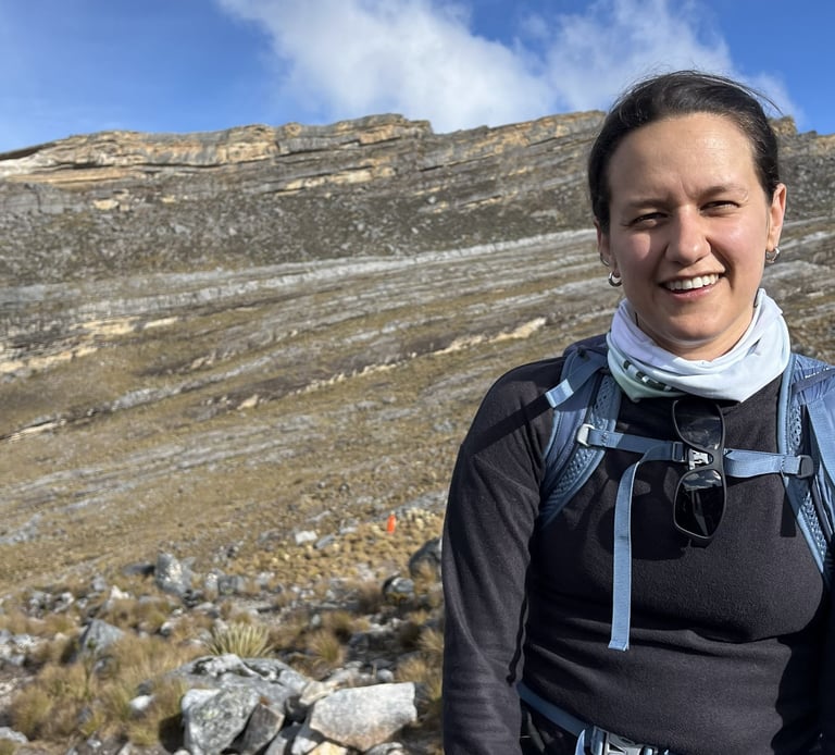 A smiling woman hiking with a backpack in a rocky mountain landscape under a blue sky.