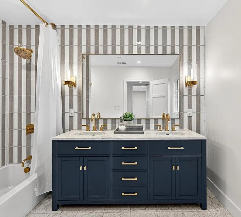 Bathroom remodel with a blue vanity, gold fixtures, and striped tile walls.