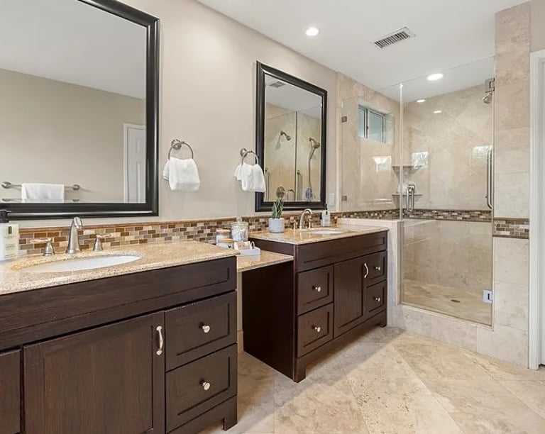 Bathroom remodel with a double vanity, framed mirrors, and stone countertops.