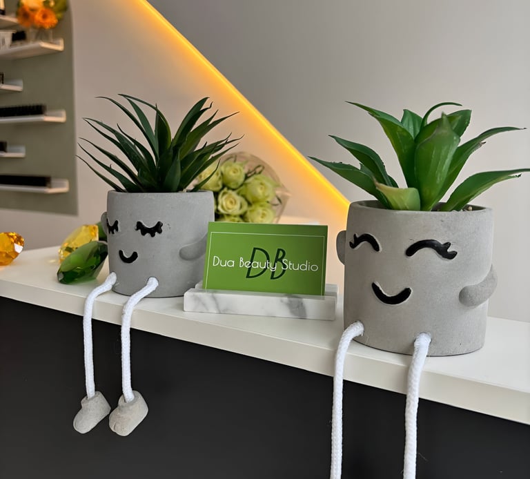 Two plant pots with a smile and a green business card with Dua Beauty Studio on it.
