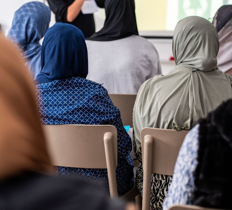 persona blanca con pelo marron y gafas en una aula enseñando un mobil a sus alumnas.