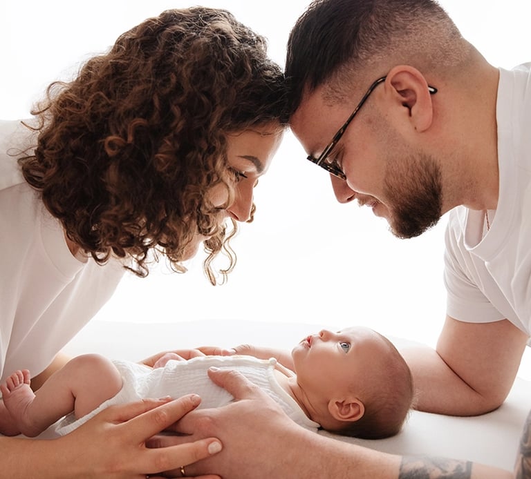 photo de bébé avec ses parents au dessus de lui et les regarde