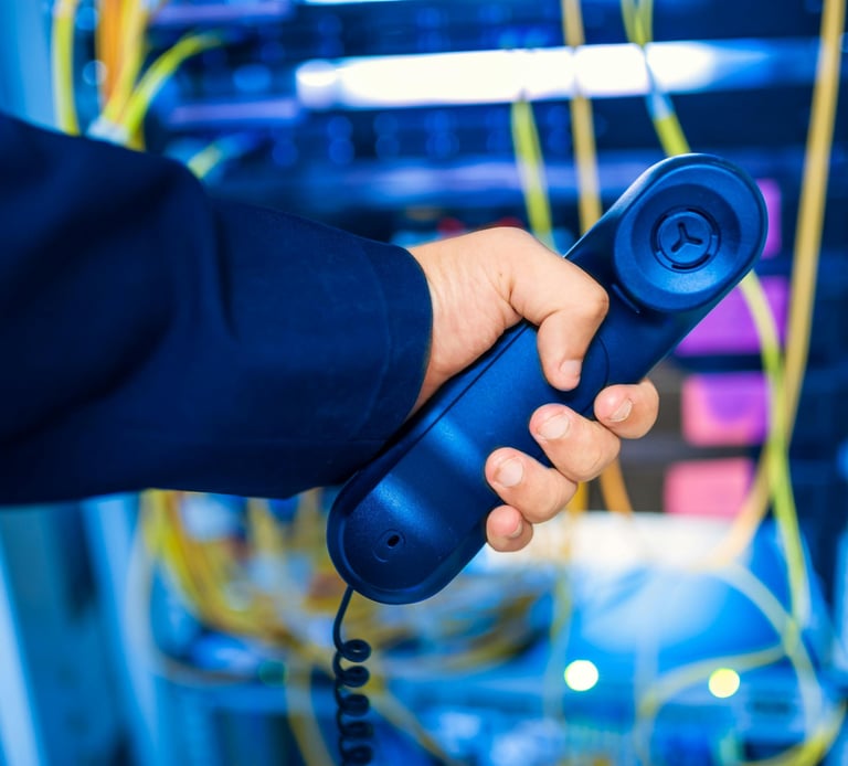 Person holding a phone behind a network rack, representing IT support and remote troubleshooting services
