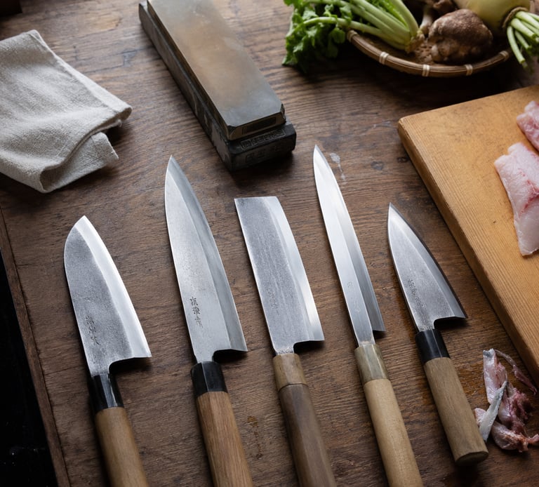 Professional Japanese chef knives and whetstone on a rustic wooden kitchen counter with fresh vegetables.