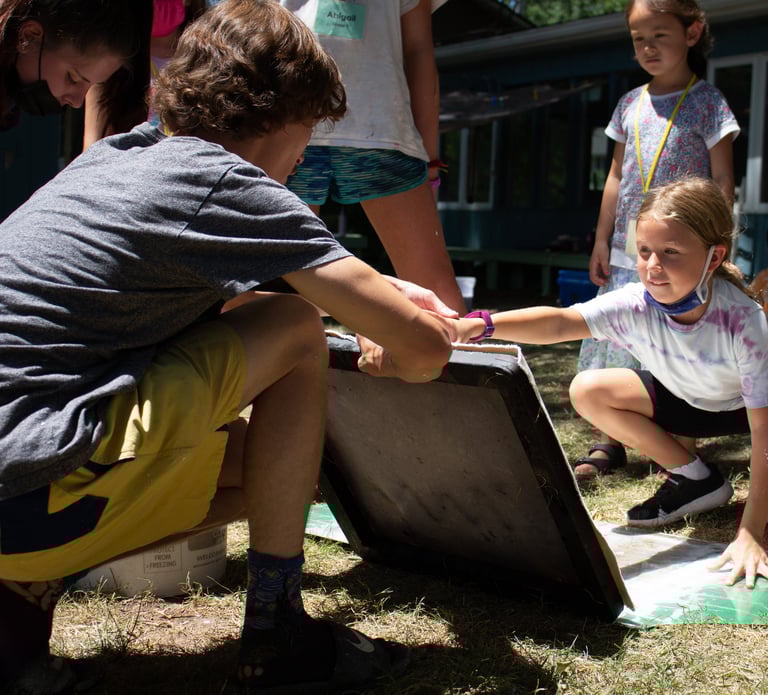 Teacher holding up a screen for papermaking in front of one of our youth students.