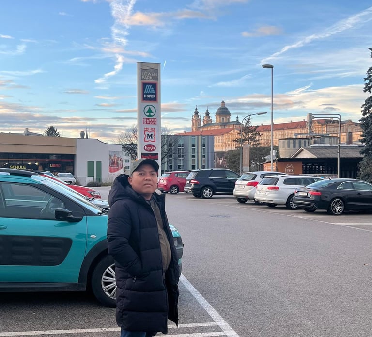 River crew stands in a busy parking lot with Melk Abbey in the background.