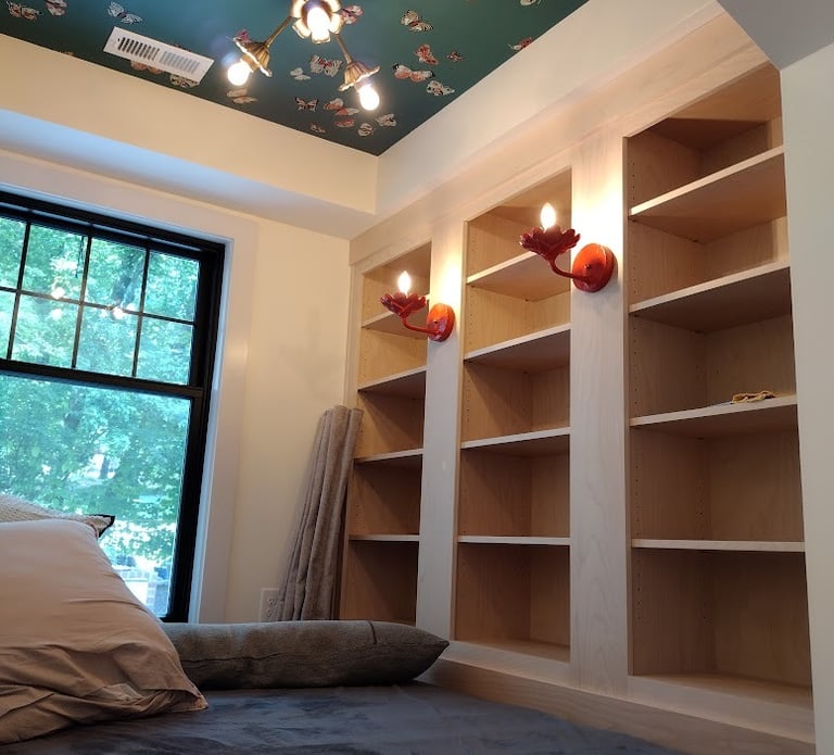 Cozy reading nook featuring built-in bookshelves, butterfly wallpaper ceiling, and red bird wall sconces.