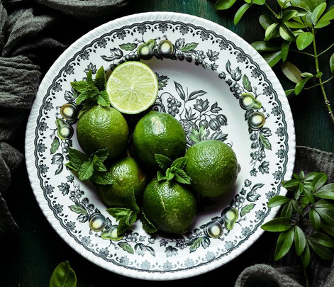 Fresh whole limes and mint leaves on a vintage floral patterned ceramic plate.