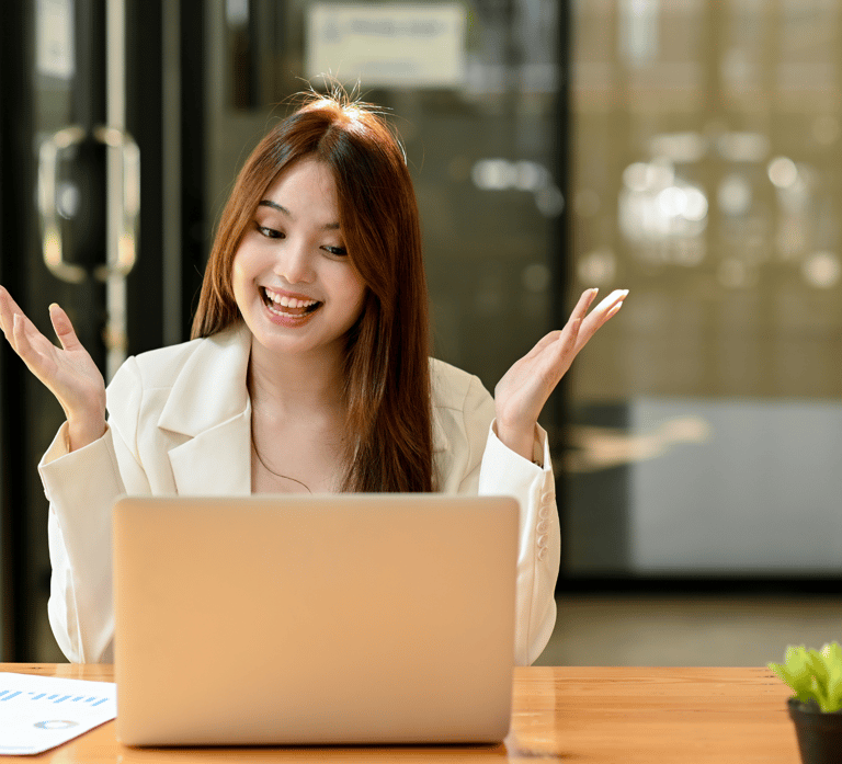 an ecstatic woman celebrating sitting at a table with a laptop and a plant