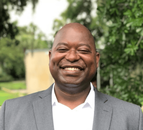 Dollar Harmony Coach Wildo in a suit and white shirt smiling