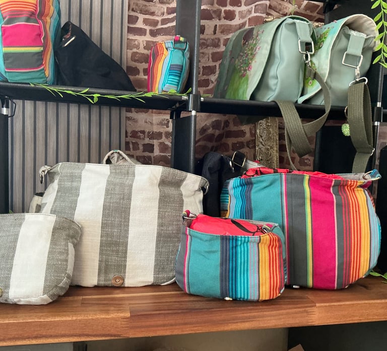 Handmade colorful striped canvas shoulder bags and crossbody purses displayed on a boutique wooden shelf.